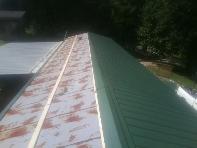 Old rusted panels beside newly installed green metal roofing — Wind Damage Roof Repair by Roofing Brothers in Eddyville