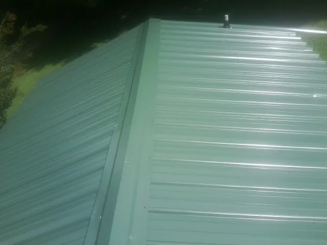 New green metal panels meeting at the ridge of a roof — Flat Roof Repair work by our crew in Eddyville