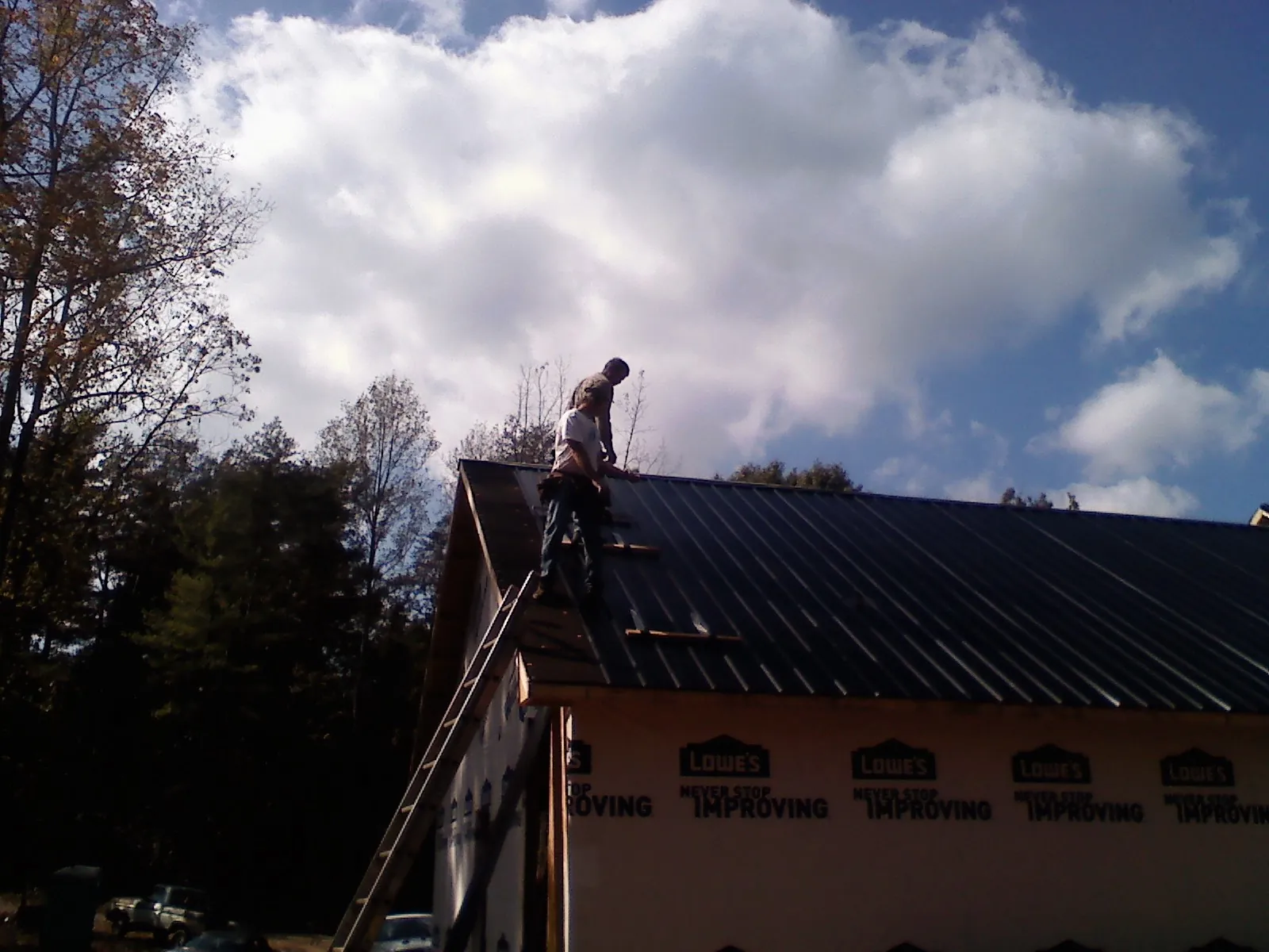 Roofer fastening dark metal panels high against a cloudy sky, from a Roof Inspection job in Eddyville
